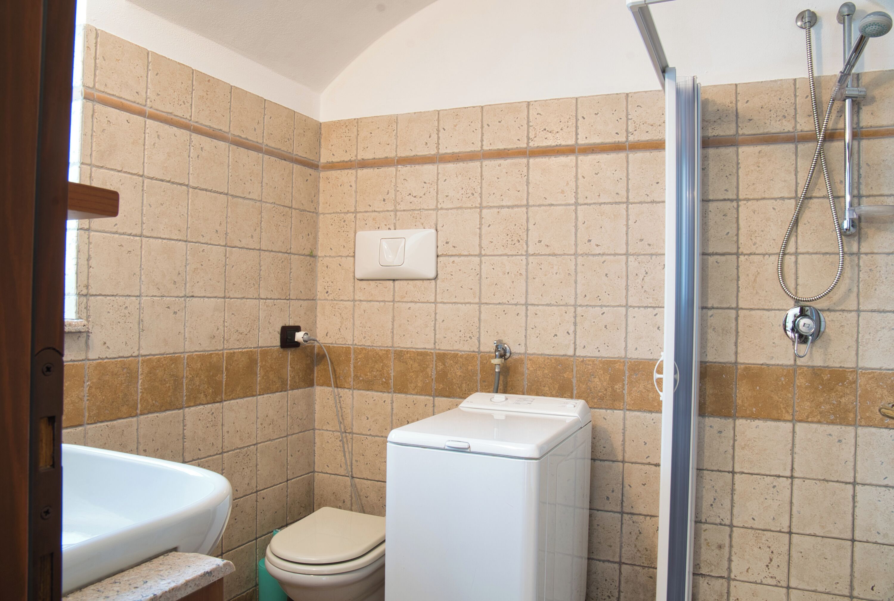 Een badkamer met toilet, wasmachine en douche.