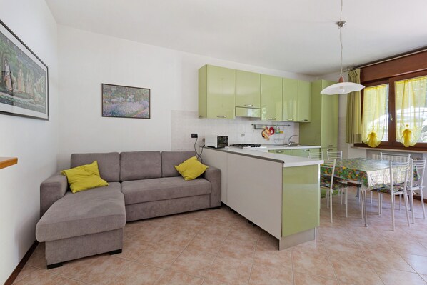 A modern living room with a sofa, a dining table with chairs, a kitchen area, and artwork on the walls.