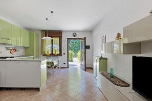 A modern kitchen with green cabinets, a dining area with chairs, a TV, and a door leading outside.