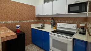 Cocina compacta con microondas, estufa, pileta y armarios azules.