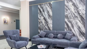 Una sala de estar moderna con un sofá gris, dos sillones y una mesa de centro de vidrio.