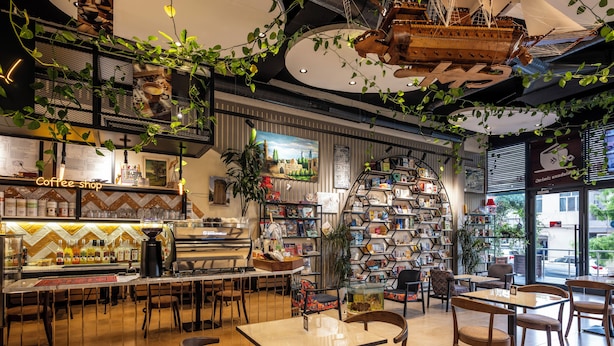 Interior de una cafetería con barra, zona de estar y una amplia estantería.