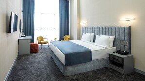 Habitación de hotel con una cama grande, un escritorio, una silla, un televisor y una ventana con cortinas.