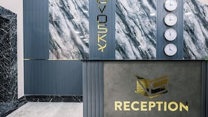 Zona de recepción con pared de mármol, franjas verticales y relojes.