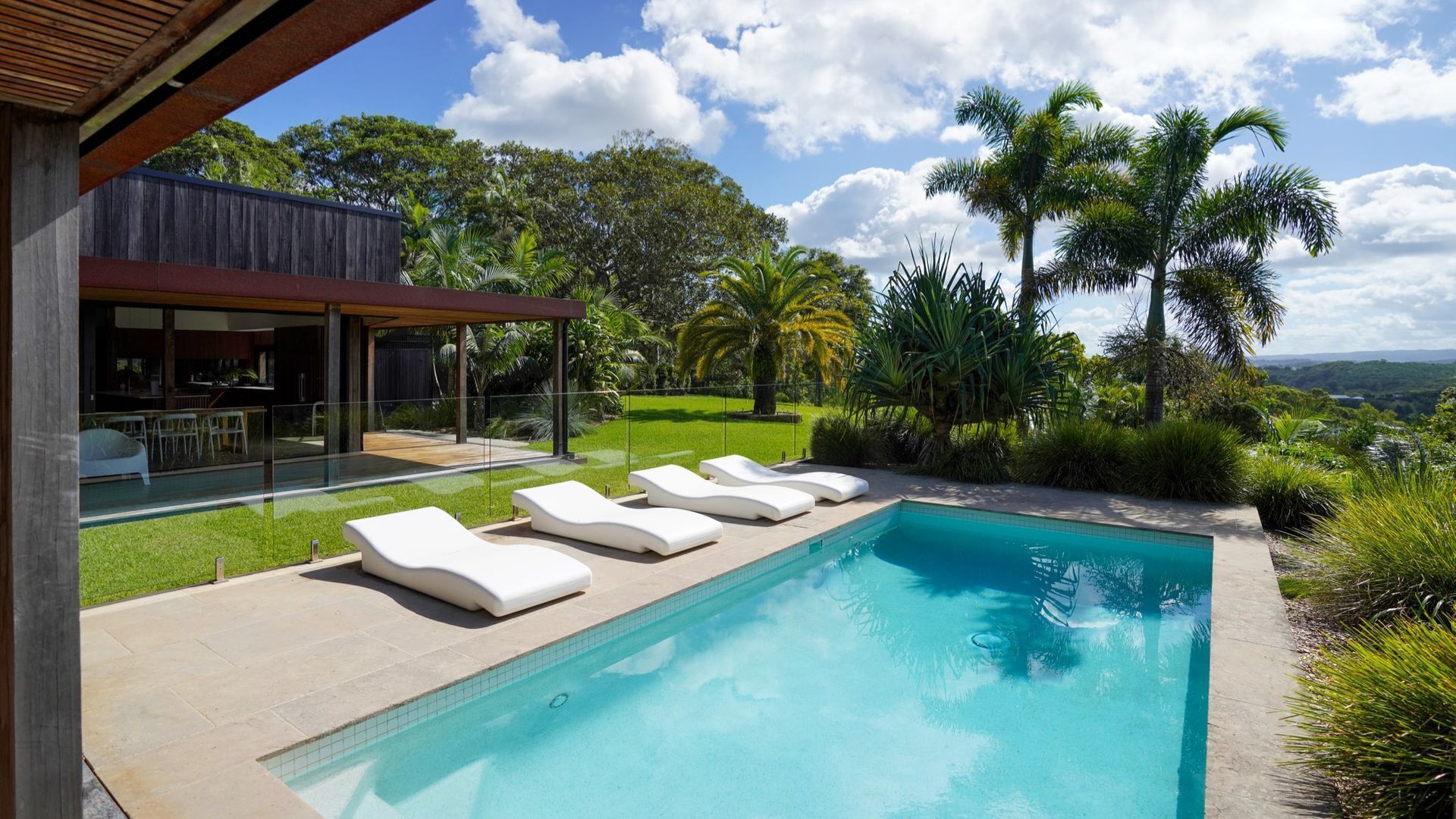 Une maison moderne dotée d’une piscine, de chaises longues blanches et d’une végétation luxuriante.