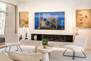 A modern living room with a fireplace, two armchairs, a coffee table, and a large painting of a coastal landscape. - Villa 'Gotmar Beach Is A Modern' with Private Pool, Wi-Fi and Air Conditioning (Pollença)