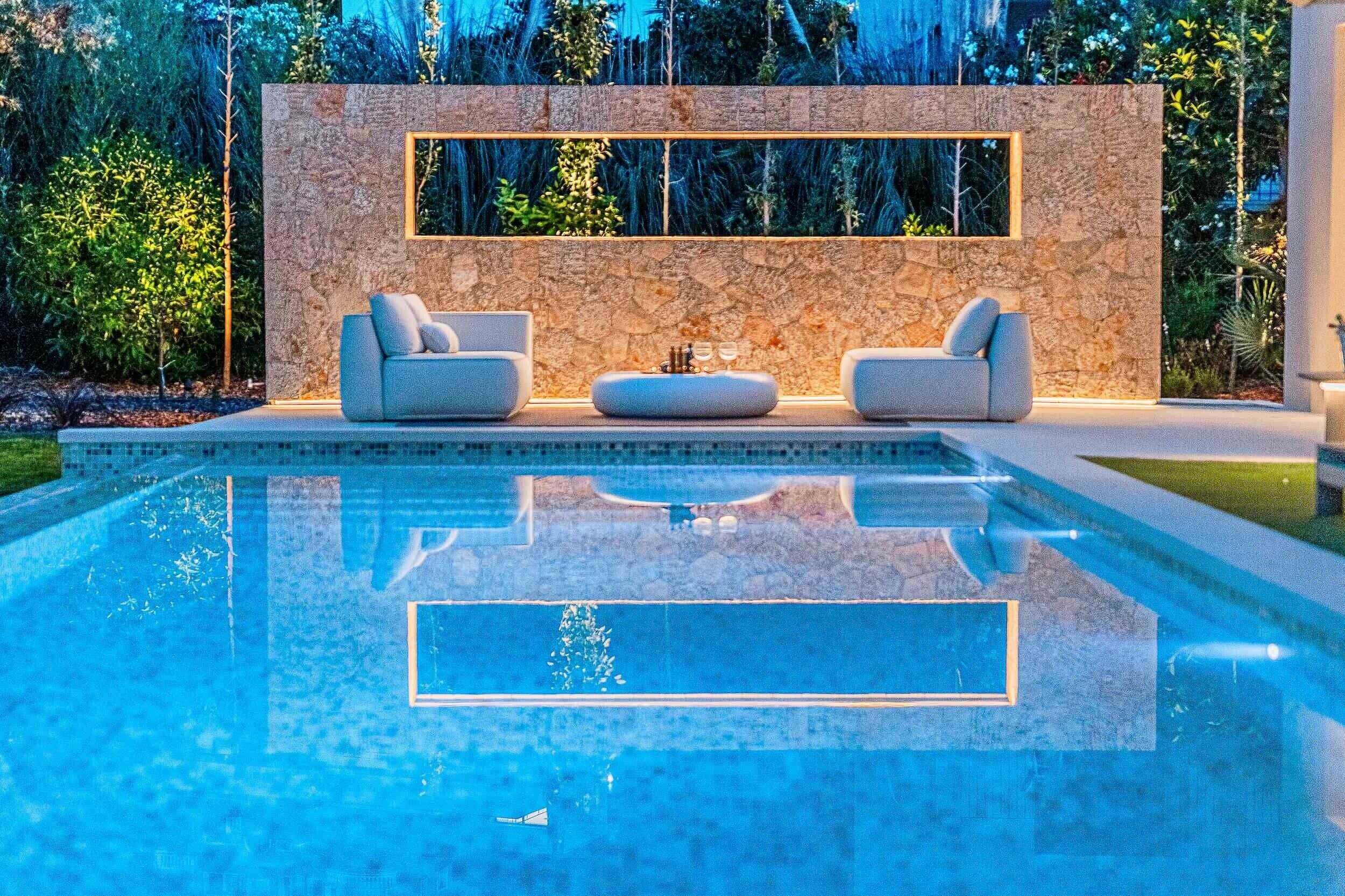 A modern pool area with a stone wall, two sofas, and a small table.