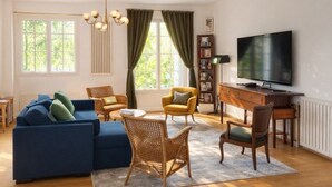 Una sala de estar con un sofá, sillas, un televisor y una estantería.