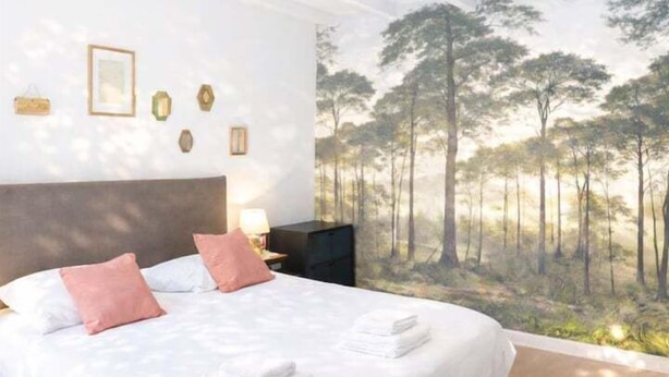 Un dormitorio con cama, mesita de noche, lámpara y un mural en la pared.