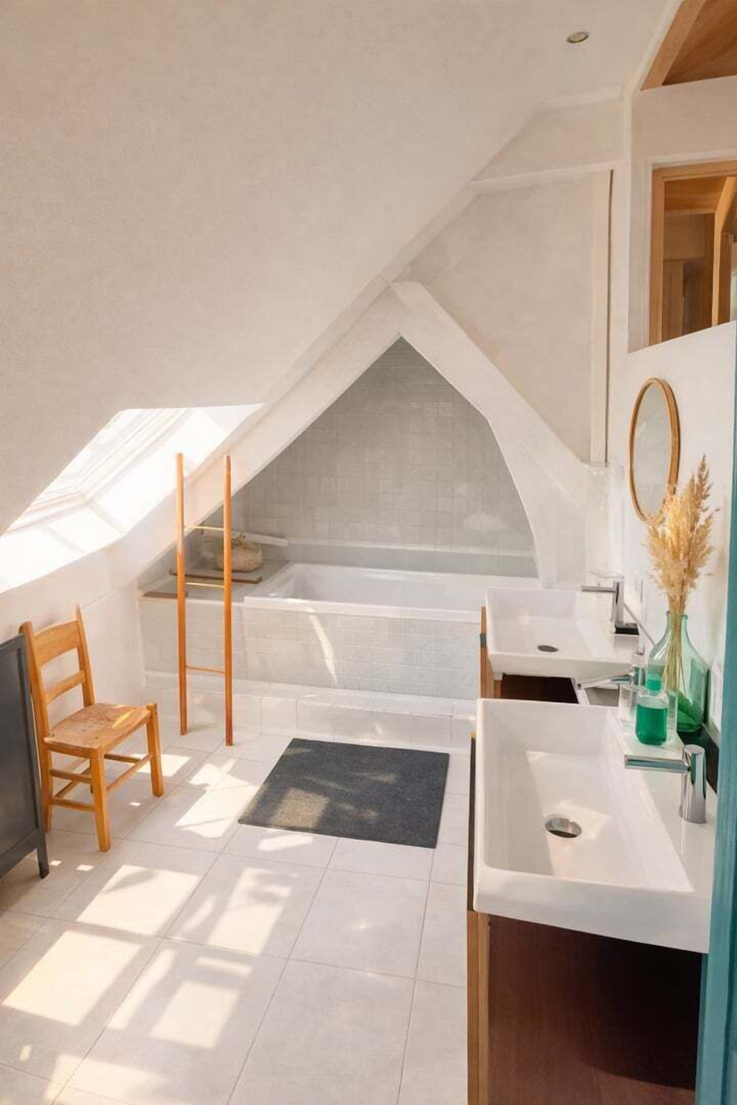 A modern bathroom with a skylight, a bathtub, a vanity with a mirror, and a wooden chair.