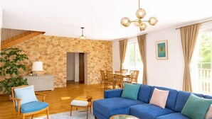 Un salón con sofá azul, sillas de madera, una mesa de centro de vidrio, pared de piedra y una escalera.