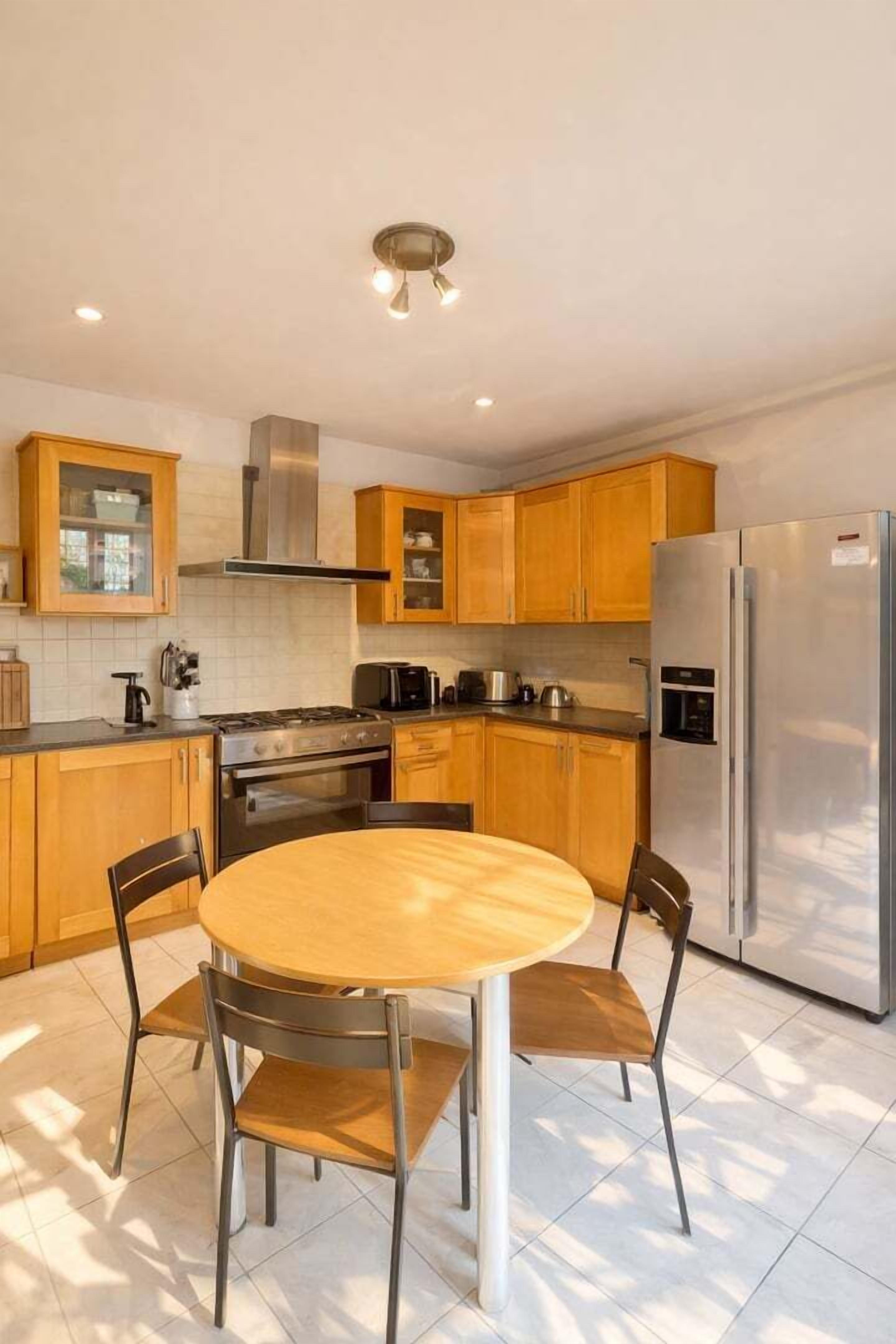 A modern kitchen with wooden cabinets, a stainless steel refrigerator, a gas stove, and a round dining table with chairs.