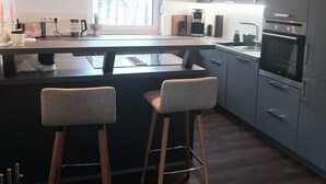 Moderni keittiö, jossa on keskeinen keittiösaareke, baarituolit, sisäänrakennettu uuni ja mikroaaltouuni.