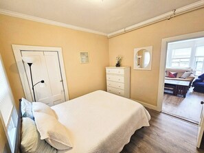 Quarto com cama, cômoda, espelho e porta que dá para uma sala.