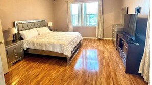 Une chambre à coucher avec un lit, des tables de chevet, une télévision et une fenêtre avec des rideaux.