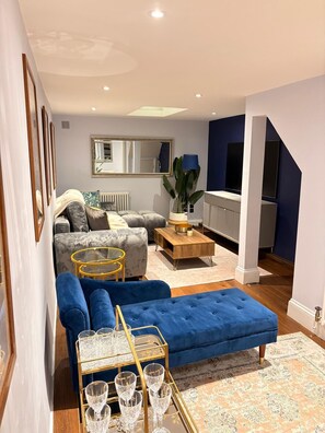 A modern living room with a blue sectional sofa, a coffee table, and a glassware display. - Stunning 4 Bed Town House w/ Roof Terrace in Farringdon / St Paul's Cathedral (London)