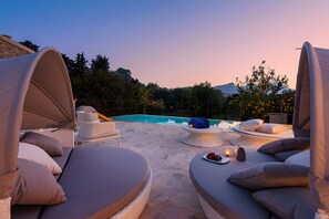 A poolside area with lounge chairs, a table with a blanket and a bottle, and a view of the pool.