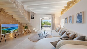A modern living room with a sofa, coffee table, TV, staircase, and artwork. - Villa 'Can Mas  Antigua' with Mountain View, Wi-Fi and Air Conditioning (Illes Balears)