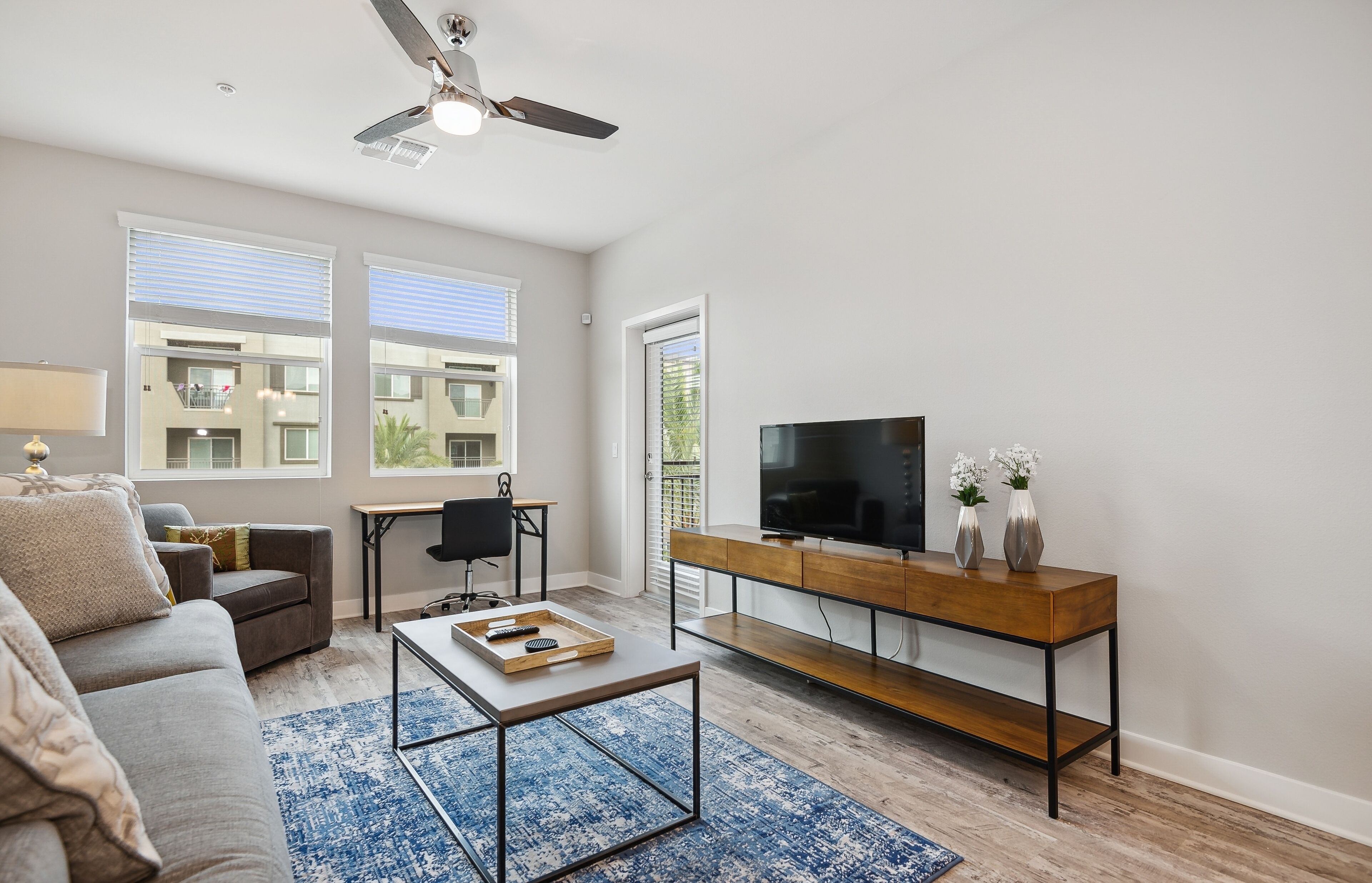 A modern living room with a sofa, coffee table, TV stand, and a ceiling fan.