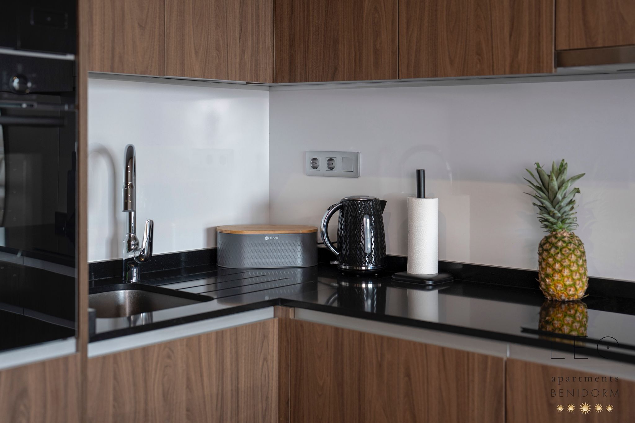 Una cucina moderna con mobili in legno, un lavello in acciaio inox, un bollitore e un'ananas sul bancone.