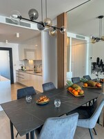 A modern dining area with a marble table, grey upholstered chairs, and a variety of fruits and pastries.