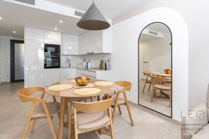 A modern kitchen with white cabinets, a round dining table with wooden chairs, and a central island with a bowl of fruit.