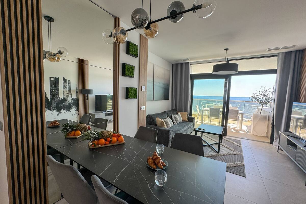 A modern living room with a dining area, a sofa, and a view of the outdoors.