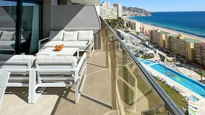 A balcony with a pool, white furniture, and a view of the beach and cityscape. - Sunset Cliffs Sea View (Benidorm)