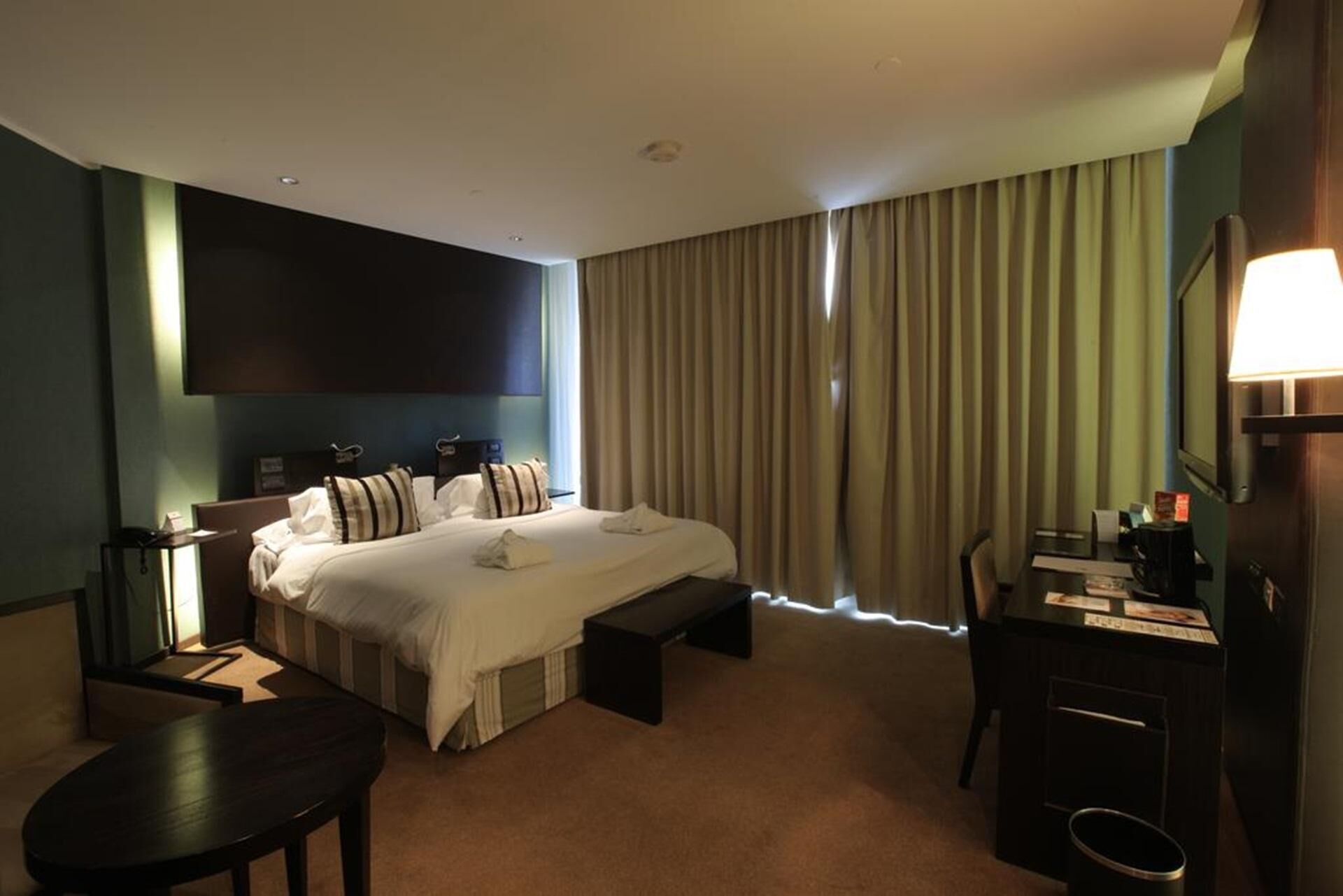 Habitación de hotel con una cama grande, un escritorio, una silla, un televisor y una ventana con cortinas.