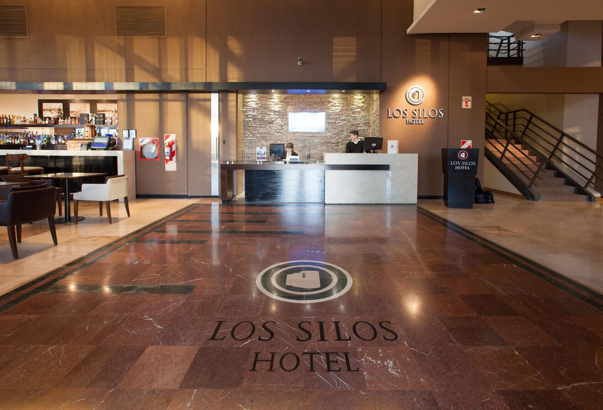 Vestíbulo de hotel con mostrador de recepción, zona de estar y escalera.