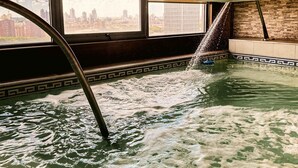 Een bubbelbad met waterstralen, een stadszicht door grote ramen en een betegelde vloer.