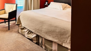 Een hotelkamer met een bed, een stoel, een nachtkastje en een raam met gordijnen.