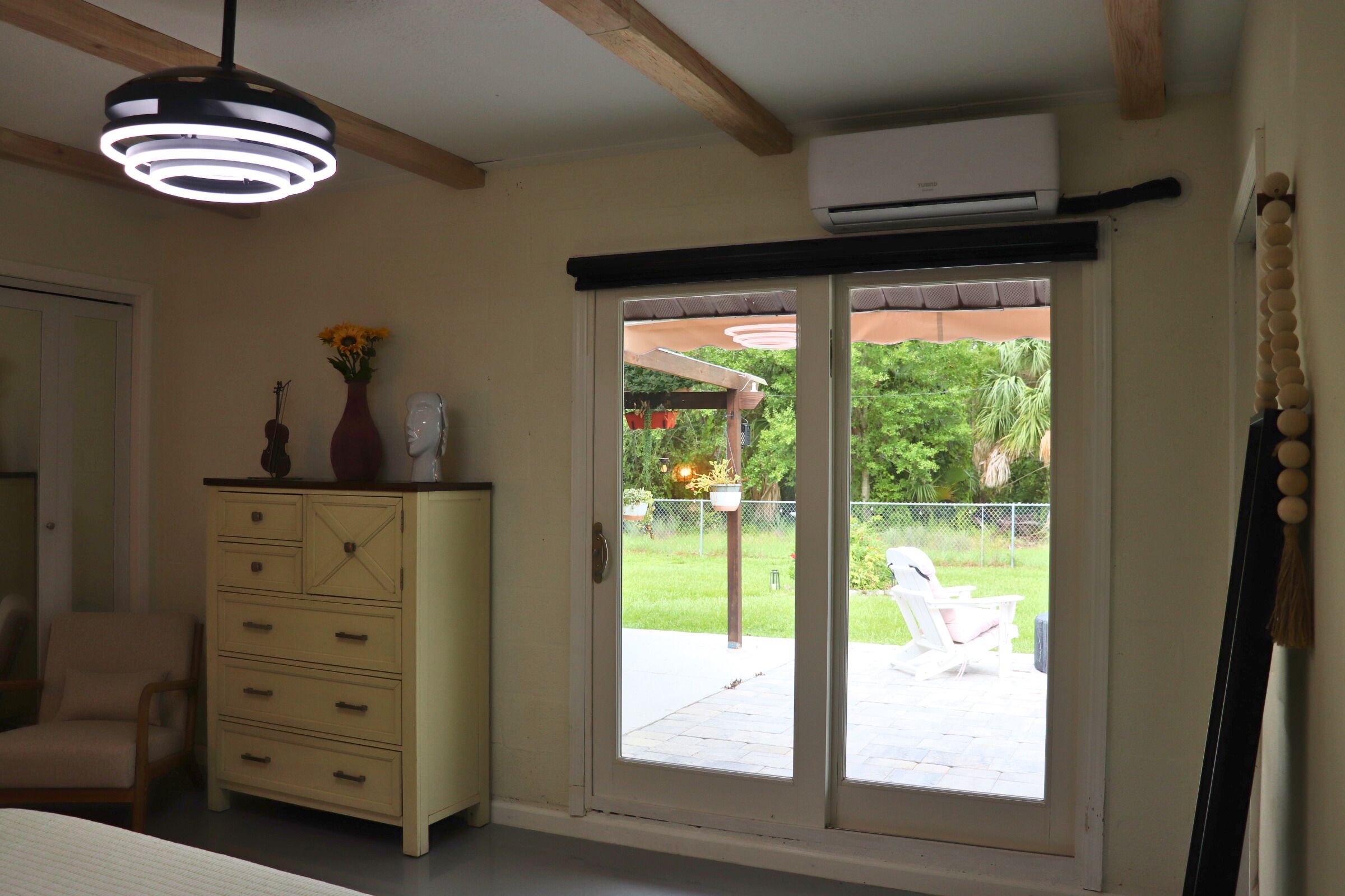A room with a sliding glass door leading to an outdoor patio, a dresser with drawers, a hanging light fixture, and an air conditioning unit mounted on the wall.