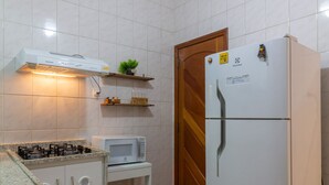 A kitchen with white tiled walls, a white refrigerator, a microwave, and a gas stove.