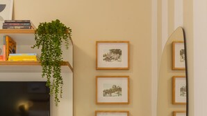 A room with a TV mounted on the wall, a bookshelf with books and a plant, framed pictures on the wall, and a mirror.