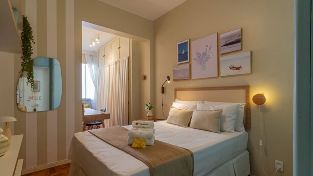 A hotel room with a large bed, a bedside table, a mirror, and a view of the dining area.
