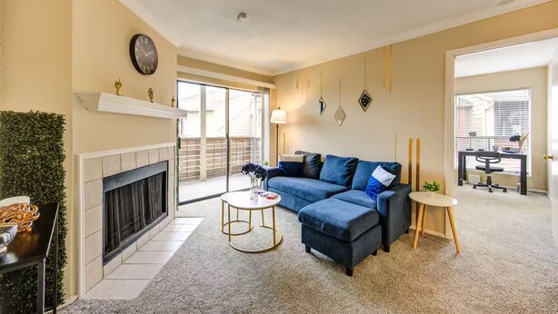 A living room with a fireplace, a blue sectional sofa, a round coffee table, and a desk with a chair. - HTX Cozy Hideaway (Houston)