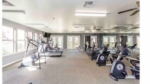 A spacious gym with multiple cardio machines, large windows, and ceiling fans. - HTX Cozy Hideaway (Houston)