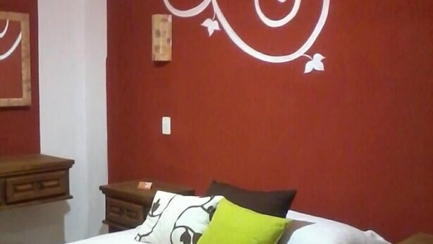 Un dormitorio con cama, almohadas, una mesita de noche y una pared decorada con espirales y mariposas.