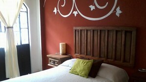 Un dormitorio con cabecera de madera, una mesita de noche con una vela y una cama con almohada blanca y verde.