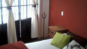 Un dormitorio con una cama, una ventana con cortinas, un radiador, una lámpara de pared y un aparador de madera.