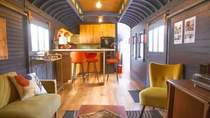 Un interior acogedor con un sofá, sillas, una mesa de centro y una zona de cocina con taburetes.