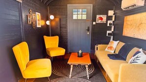 Una habitación acogedora con una pared oscura, piso de madera, sofá amarillo, sillón amarillo y una mesita con lámpara.