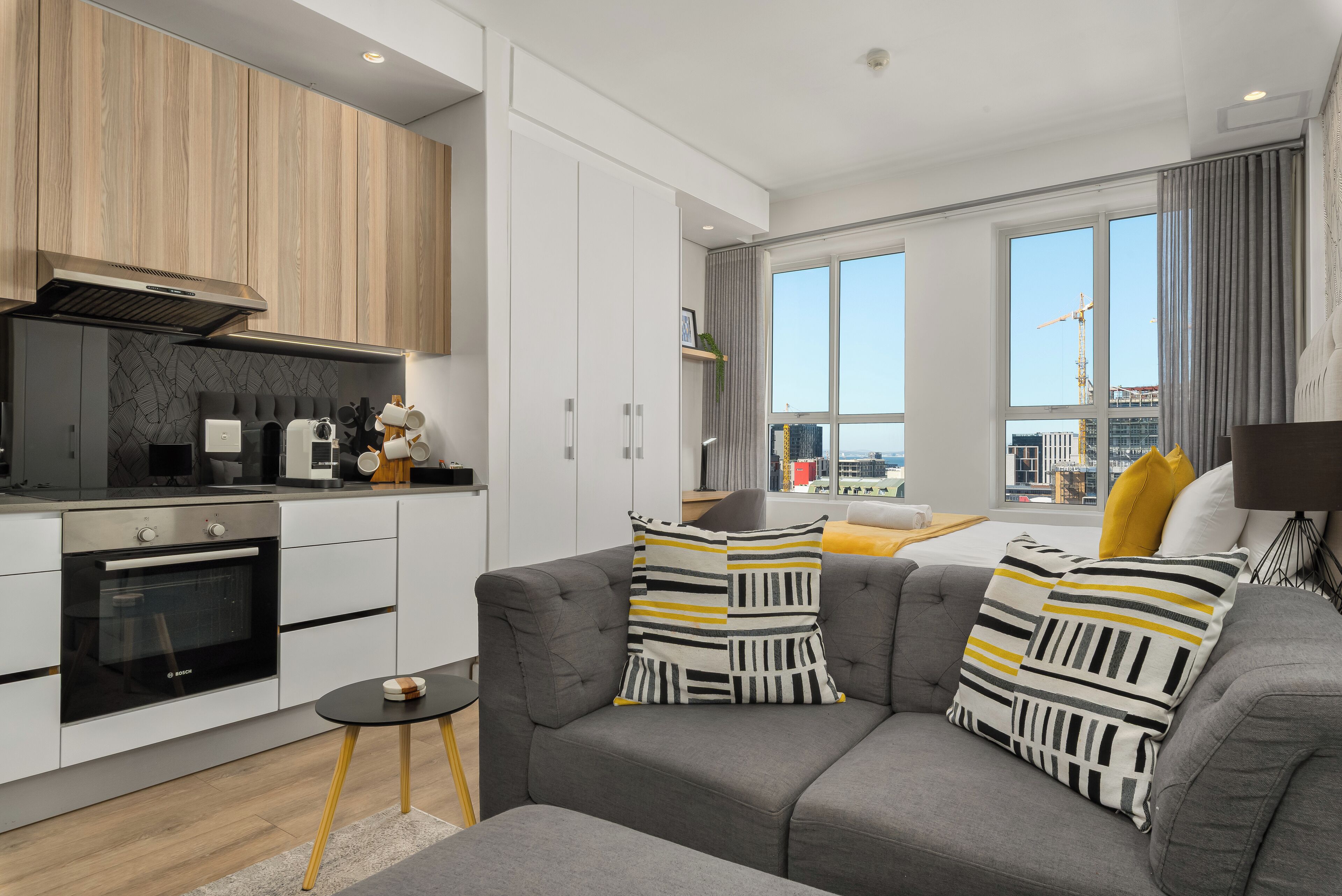 Een modern appartement met een keuken, een grijze bank en grote ramen.