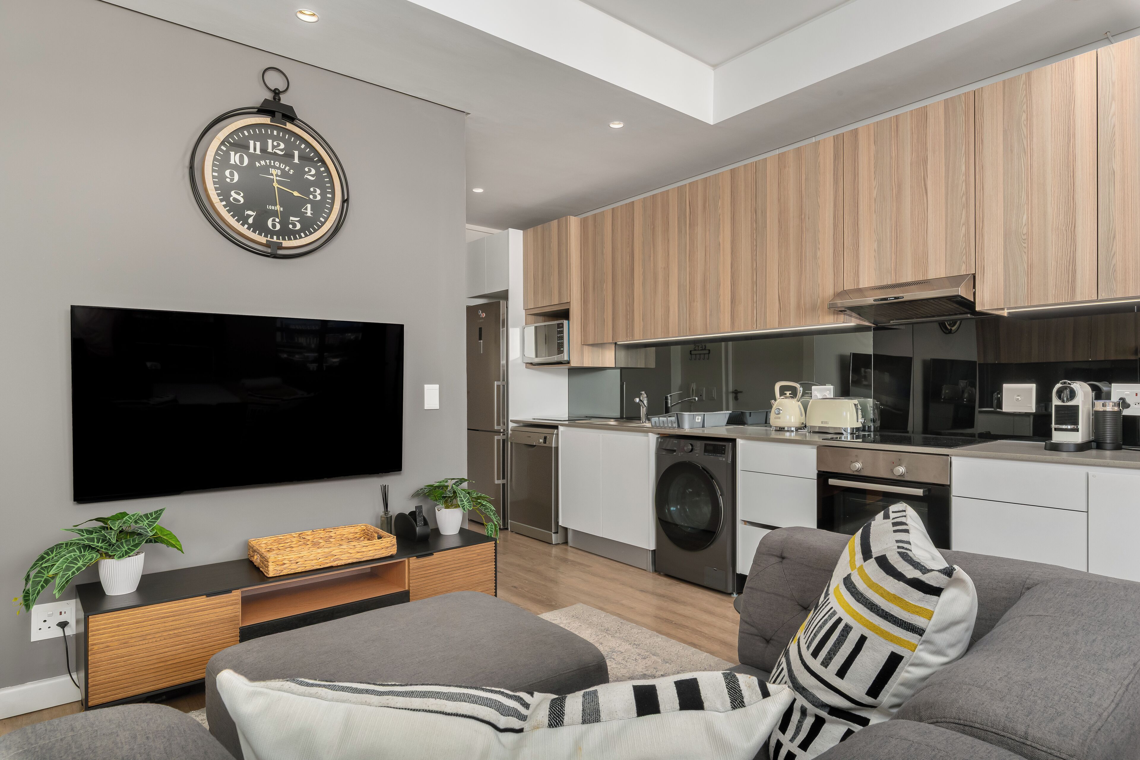Una cocina moderna con electrodomésticos integrados, un televisor de pantalla plana y una zona de comedor con sofá y cojines.