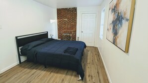 Une chambre avec un lit, un mur en briques, une porte blanche et un tableau accroché au mur.