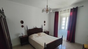 Une chambre à coucher avec un lit en bois, une table de chevet, un lustre et une fenêtre avec des rideaux.