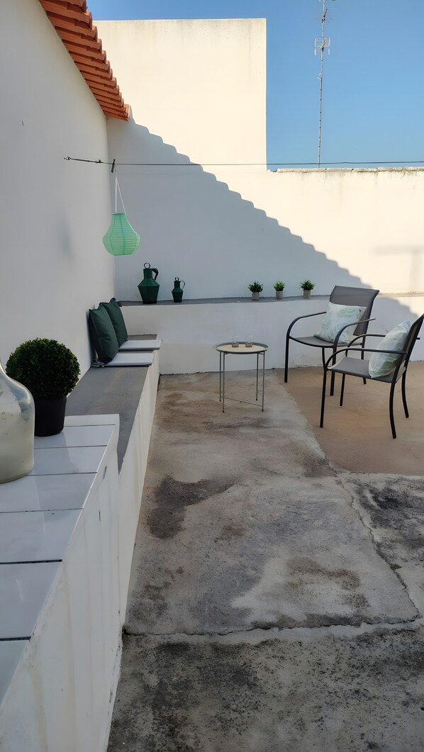 A rooftop terrace with a seating area, a table, and potted plants.
