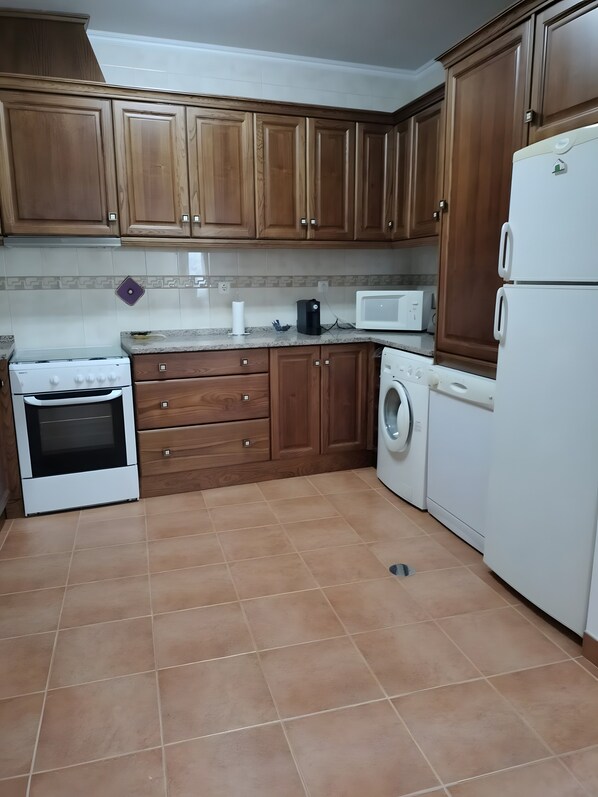A kitchen with wooden cabinets, a stove, a microwave, and a washing machine.
