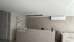 A reception desk with a sign reading "AUREA" in a modern, minimalist lobby with a tiled floor and a sofa in the background. - Flat Cabo Branco Aurea 50m do mar 105 (Joao Pessoa)